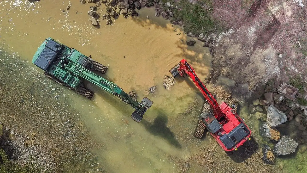Aerial view of two excavators working beside water on a rural site