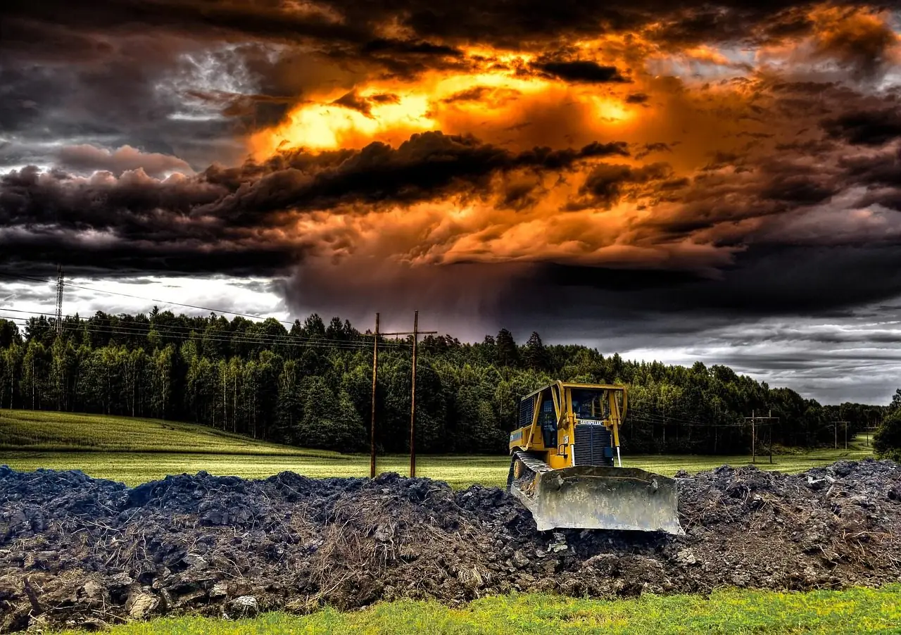 Bulldozer on churned ground under a dramatic stormy sky