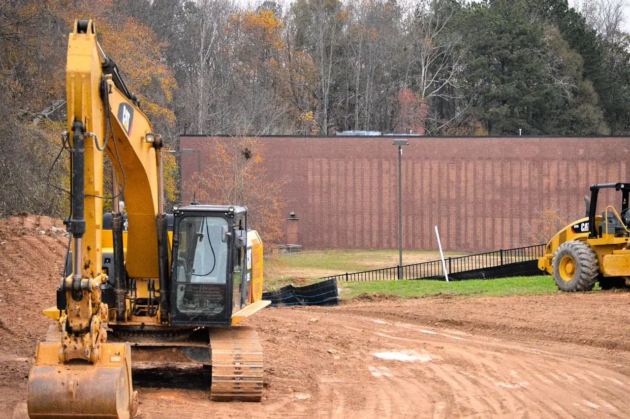 Yellow excavator digging red clay beside a building